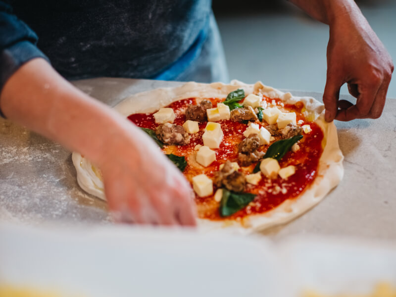 A person is standing at a table picking up a handmade pizza